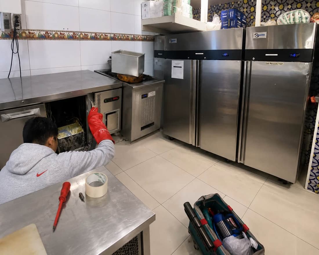 Técnico de Clima Frío reparando una nevera industrial de acero inoxidable en la cocina de un restaurante en Lechería